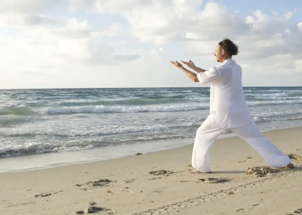 sund livsstil og resiliens - mand i hvidt udfører Tai Chi på strand